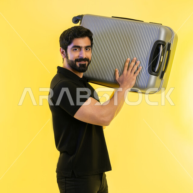 السياحة في إجازة الصيف، الاستعداد لقضاء رحلة صيفية ترفيهية ممتعة، بورتريه مقرب لشاب عربي خليجي اماراتي يرتدي الزي الكاجوال يحمل حقيبة السفر على كتفه، النظر إلى الكاميرا بإيماءات الحماس، الشعور بالسعادة والفرح، خلفية صفراء