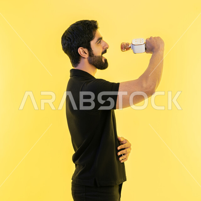 ممارسة موهبة الغناء، تقديم العروضات المسرحية، إيماءات وتعابير الاندماج والتفاعل مع الموسيقا، الاستمتاع بأداء المواهب الصوتية، بورتريه من الجانب لشاب عربي خليجي اماراتي يرتدي الزي الكاجوال يمسك بيده المايكروفون، تسجيل مقطع صوتي غنائي، خلفية صفراء