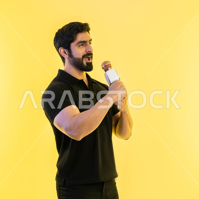 الاستمتاع بأداء المواهب الصوتية، ممارسة موهبة الغناء، تقديم العروضات المسرحية، إيماءات وتعابير الاندماج والتفاعل مع الموسيقا، بورتريه من الجانب لشاب عربي خليجي اماراتي يرتدي الزي الكاجوال يمسك بيده المايكروفون، تسجيل مقطع صوتي غنائي، خلفية صفراء