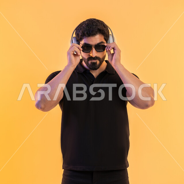 مواهب غنائية فنية، إيماءات وتعابير الاندماج مع الأغنية، التفاعل مع الانغام الموسيقية، الإستماع للأغاني بإستخدام الهيدفون، بورتريه لرجل عربي خليجي اماراتي يرتدي الزي الكاجوال والنظارات الشمسية يضع سماعة الرأس في استديو صوتي، خلفية بيج