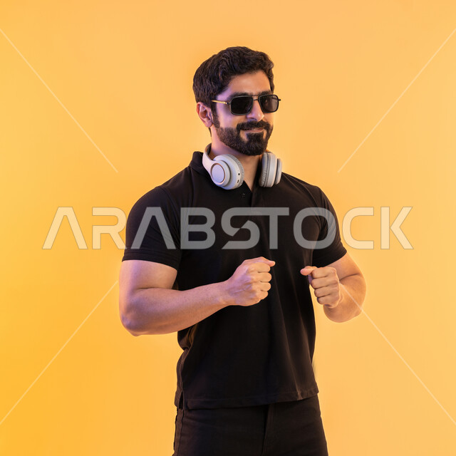 إيماءات وتعابير الاندماج مع الأغنية، التفاعل مع الانغام الموسيقية، الإستماع للأغاني بإستخدام الهيدفون، مواهب غنائية فنية، بورتريه لرجل عربي خليجي اماراتي يرتدي الزي الكاجوال والنظارات الشمسية يضع سماعة الرأس في استديو صوتي، خلفية بيج