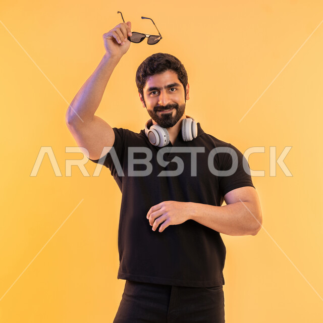 التفاعل مع الانغام الموسيقية، إيماءات وتعابير الاندماج مع الأغنية، مواهب غنائية فنية، بورتريه لشاب عربي خليجي اماراتي يرتدي الزي الكاجوال يضع سماعة الرأس في استديو صوتي يحمل بيده نظارات شمسية، الإستماع للأغاني بإستخدام الهيدفون، خلفية بيج