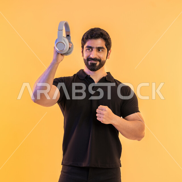 مواهب غنائية فنية، التفاعل مع الانغام الموسيقية، إيماءات وتعابير الاندماج مع الأغنية، بورتريه لشاب عربي خليجي اماراتي يرتدي الزي الكاجوال  يحمل بيده سماعة الرأس في استديو صوتي، الإستماع للأغاني بإستخدام الهيدفون، خلفية بيج