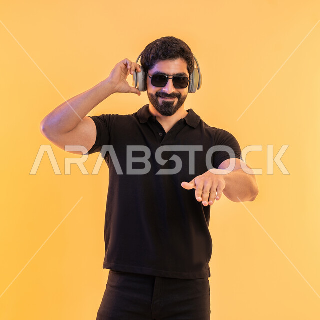 التفاعل مع الانغام الموسيقية، إيماءات وتعابير الاندماج مع الأغنية، مواهب غنائية فنية،بورتريه لشاب عربي خليجي اماراتي يرتدي الزي الكاجوال والنظارات الشمسية يضع سماعة الرأس في استديو صوتي، الإستماع للأغاني بإستخدام الهيدفون، خلفية بيج