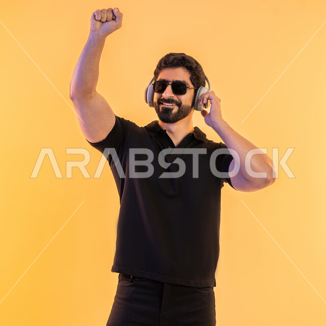 إيماءات وتعابير الاندماج مع الأغنية، مواهب غنائية فنية،بورتريه لشاب عربي خليجي اماراتي يرتدي الزي الكاجوال والنظارات الشمسية يضع سماعة الرأس في استديو صوتي، الإستماع للأغاني بإستخدام الهيدفون، التفاعل مع الانغام الموسيقية، خلفية بيج