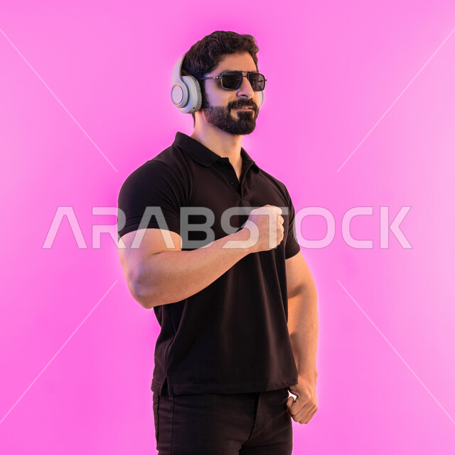 مواهب غنائية فنية، إيماءات وتعابير الاندماج مع الأغنية، بورتريه من الجانب لشاب عربي خليجي اماراتي يرتدي الزي الكاجوال والنظارات الشمسية يضع سماعة الرأس في استديو صوتي، الإستماع للأغاني بإستخدام الهيدفون، التفاعل مع الانغام الموسيقية، خلفية وردية