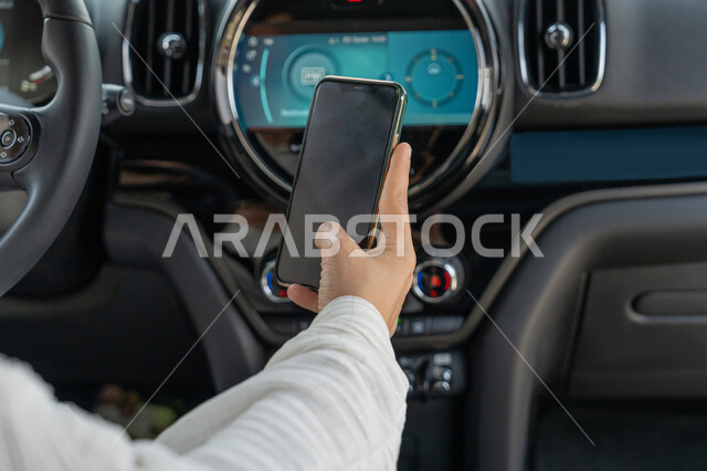 القيادة في الطرق والشوارع العامة، صورة مقربة ليد سيدة عربية خليجية إماراتية تقوم بتتبع الطريق عبر الانترنت، اعتماد المرأة على نفسها في التنقل والمواصلات، شابة سعودية تجلس داخل سيارتها تحمل الهاتف المحمول، مفهوم الاستقلال والاعتماد على النفس