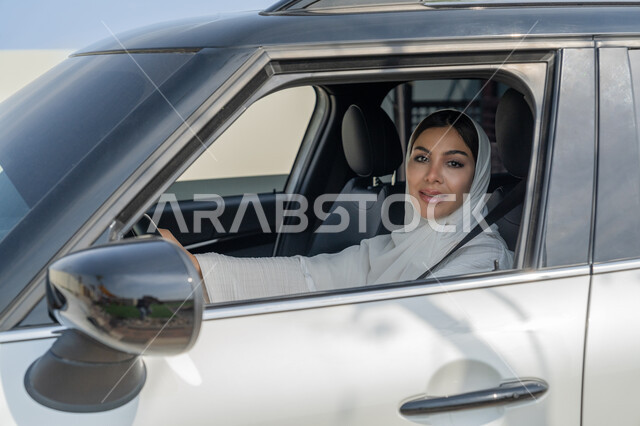 وضع حزام الأمان والجلوس داخل السيارة، تطبيق مفهوم الأمان والحماية، الاعتماد على النفس عند المرأة العربية في التنقل و المواصلات، إمرأه عربية خليجية إماراتية محجبة تجلس داخل سيارتها، سيدة سعودية تنظر إلى الكاميرا بإيماءات البشاشة، حرية القيادة للمرأة الخليجية
