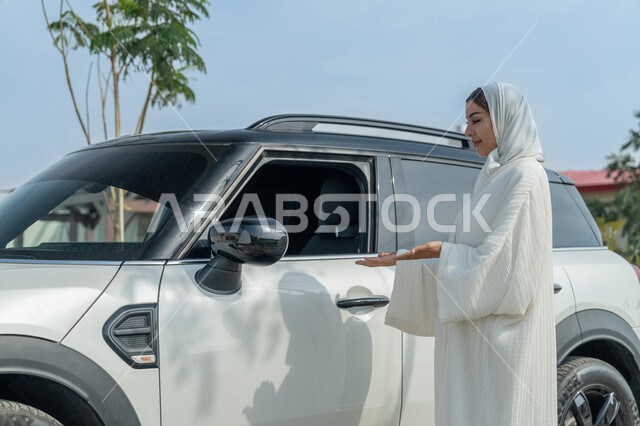 الإشارة إلى السيارة بإيماءات الثقة بالنفس, حرية قيادة المركبات للمرأة العربية, شابة عربية خليجية إماراتية تلبس العباءة البيضاء, سيدة سعودية تقف بجانب سيارتها, مفهوم الاستقلال عند الأنثى الخليجية، الاعتماد على النفس في المواصلات والتنقل عند الامرأة