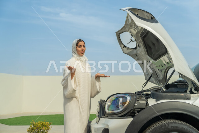 الحيرة وعدم معرفة سبب المشكلة, اعتماد المرأة على نفسها في التنقل و المواصلات، إمرأه عربية خليجية إماراتيه محجبة ترتدي العباءة تقف أمام السيارة بمحاولة لاكتشاف العطل، حرية القيادة للمرأة الخليجية، شابة سعودية تفتح يديها بقلق, الاستقلال عند المرأة العربية