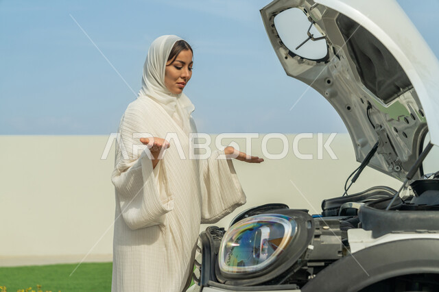 فتح اليدين بإيماءات الحيرة وعدم معرفة المشكلة, اعتماد المرأة على نفسها في التنقل و المواصلات، إمرأه عربية خليجية إماراتيه محجبة ترتدي العباءة تحاول اكتشاف العطل، حرية القيادة للمرأة الخليجية، شابة سعودية تقف أمام السيارة بحيرة, الاستقلال عند المرأة العربية