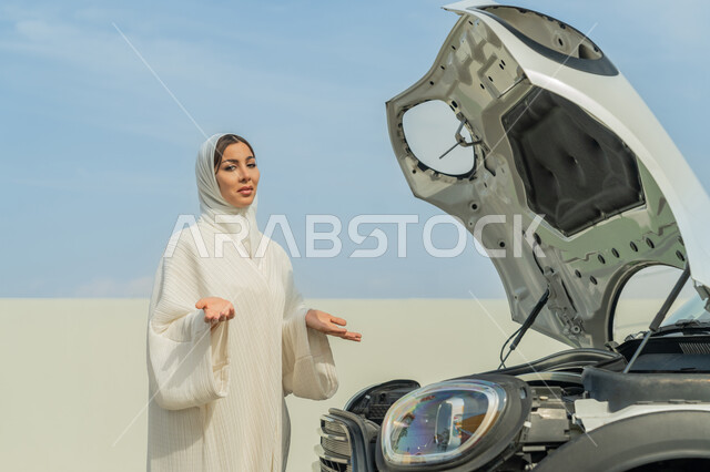 مفهوم الاستقلال للمرأة العربية، اعتماد المرأة على نفسها في التنقل و المواصلات، سيدة عربية خليجية إماراتية محجبة تفتح يديها بإيماءات الحيرة، شابة سعودية ترتدي العباءة البيضاء, حرية القيادة للمرأة الخليجية، الوقوف أمام السيارة ومواجهة الأعطال الميكانيكية