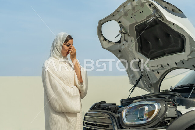 مواجهة الأعطال الميكانيكية, اعتماد المرأة على نفسها في التنقل و المواصلات، مفهوم الاستقلال للمرأة العربية، سيدة عربية خليجية إماراتية محجبة تقف بإيماءات القلق، فتح غطاء السيارة والوقوف أمامه, شابة سعودية ترتدي العباءة البيضاء, حرية القيادة للمرأة الخليجية
