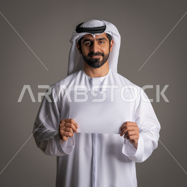 إعلان أبيض فارغ، استخدام لوحات توضيحية، مفهوم الإعلان والتسويق، موك اب أبيض، بورتريه مقرب لرجل عربي خليجي إماراتي مبتسم يرتدي الكندورة والغترة ينظر للكاميرا، خلفية رمادية