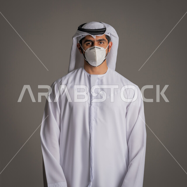اتباع إجراءات السلامة للوقاية من العدوى, توخي الحذر من انتشار فيروس كورونا, بورتريه لرجل عربي خليجي إماراتي يلبس الكندورة الاماراتية والغترة ويرتدي الكمامة الطبية, الحيطة من انتقال المرض, ارتداء القناع لإيقاف عدوى كوفيد 20, خلفية رمادية