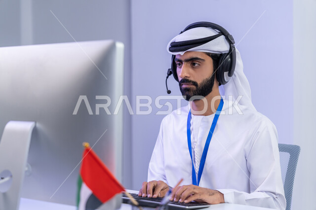 Integrating modern technologies into practical life, source of work in customer service, pride in belonging to the UAE, close-up portrait of an Arab Gulf Emirati employee wearing traditional dress sitting in the office working on a computer, gray background