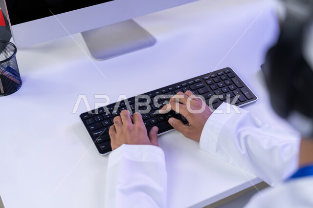 مصدر العمل في مجال خدمة الزبائن، اعداد وتقديم البرامج الإذاعية، الإجابة على أسئلة العملاء، بورتريه مقرب لأيدي موظف عربي خليجي اماراتي يرتدي الزي التقليدي يجلس في المكتب يعمل على جهاز الحاسوب، دمج التقنيات الحديثة في الحياة العملية
