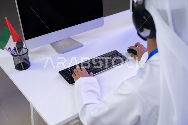 تقديم البرامج الإذاعية، دمج التقنيات الحديثة في الحياة العملية، مفهوم العمل في مجال خدمة الزبائن، الاعتزاز في الانتماء لدولة الإمارات، الإجابة على أسئلة العملاء، بورتريه مقرب لأيدي موظف عربي خليجي اماراتي يرتدي الزي التقليدي يجلس في المكتب يعمل على الحاسوب