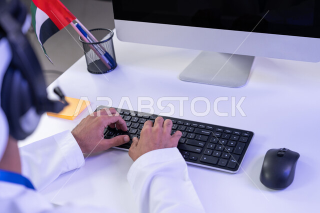 الاعتزاز في الانتماء لدولة الإمارات، مفهوم العمل في مجال خدمة الزبائن، اعداد وتقديم البرامج الإذاعية، بورتريه مقرب لأيدي موظف عربي خليجي اماراتي يرتدي الزي التقليدي يجلس في المكتب يعمل على جهاز الحاسوب، دمج التقنيات الحديثة في مجال الحياة العملية