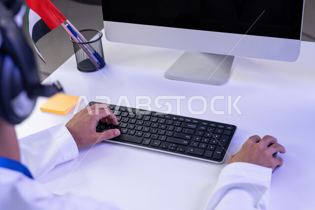 دمج التقنيات الحديثة في الحياة العملية، اعداد وتقديم البرامج الإذاعية، مفهوم العمل في مجال خدمة الزبائن، الإجابة على أسئلة العملاء، بورتريه مقرب لأيدي موظف عربي خليجي اماراتي يرتدي الزي التقليدي يجلس في المكتب يعمل على جهاز الحاسوب
