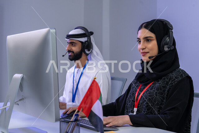 ايماءات البهجة و السرور، الفخر في الانتماء لدولة الإمارات، استخدام الأجهزة التقنية الحديثة، بورتريه مقرب لموظفيين عربيين خليجيين اماراتيين يجلسان في المكتب يقومان بالتعاون والتشارك في اداء المهام، مساهمة النساء في الوظائف المكتبية، خلفية رمادية