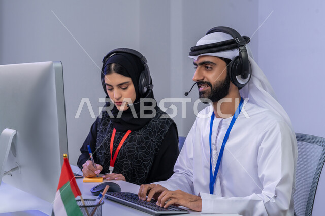 ايماءات البهجة والسرور، مفهوم العمل في مجال خدمةالزبائن، الفخر والانتماء لدولة الإمارات، بورتريه مقرب لموظفيين عربيين خليجيين اماراتيين يجلسان في المكتب يقومان بالتعاون والتشارك في اداء المهام، مشاركة النساء في الوظائف المكتبية، خلفية رمادية