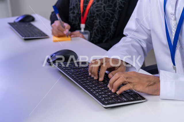 مفهوم العمل في مجال خدمة الزبائن، اعداد وتقديم البرامج الإذاعية، الإجابة على أسئلة العملاء، بورتريه مقرب لأيدي موظف عربي خليجي اماراتي يرتدي الغترة و الكندورة يجلس في المكتب يقوم باداءالمهام