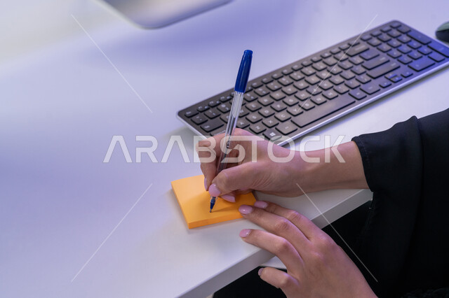 القيام بأداء المهام اليومية، الإجابة على أسئلة العملاء، مساهمة النساء في الوظائف المكتبية، مفهوم العمل في مجال خدمة الزبائن، استخدام الأجهزة الحديثة، بورتريه مقرب لأيدي موظفة عربية خليجية اماراتية تجلس في المكتب تقوم بتدوين الملاحظات على ملصقات الورق الملون