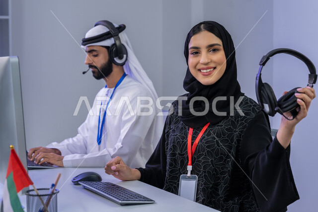الفخر والانتماء لدولة الإمارات، ايماءات البهجة والسرور، مفهوم العمل في مجال خدمة الزبائن، بورتريه مقرب لموظفيين عربيين خليجيين اماراتيين يجلسان في المكتب يقومان بالتعاون والتشارك في اداء المهام، مساهمة النساء في الوظائف المكتبية، خلفية رمادية