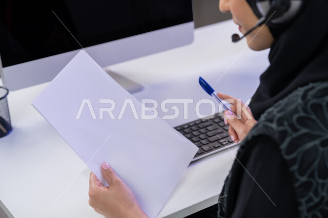 مساهمة النساء في الوظائف المكتبية، مفهوم العمل في مجال خدمة الزبائن، استخدام الأجهزة التقنية الحديثة، الإجابة على أسئلة العملاء، بورتريه مقرب لموظفة عربية خليجية اماراتية تجلس في المكتب تحمل بيدها مجموعة من الأوراق، القيام بأداء المهام اليومية