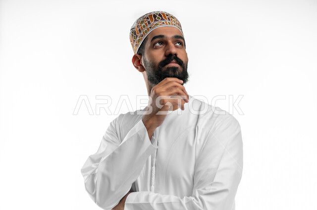 التأمل و التخطيط للمستقبل,  بورتريه مقرب  لرجل عربي خليجي عماني يرتدي الدشداشة والكمه يضعيده على ذقنه بايماءات التفكير و التركيز، ايجاد حل لمشكلة ما, تعابير شرود الذهن و التمعن, خلفية بيضاء