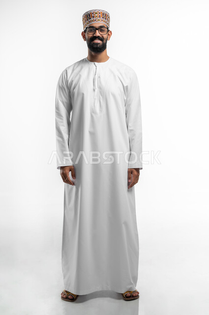 مفهوم تحسين الرؤية و محاولة تعديل البصر, إيماءات السعادة و السرور بوضوح الصورة, الرؤية من خلال العدسات الطبية, بورتريه لشاب عربي خليجي عماني يرتدي النظارة الخاصة بضعف النظر، صورة الجسم بالطول الكامل, خلفية بيضاء