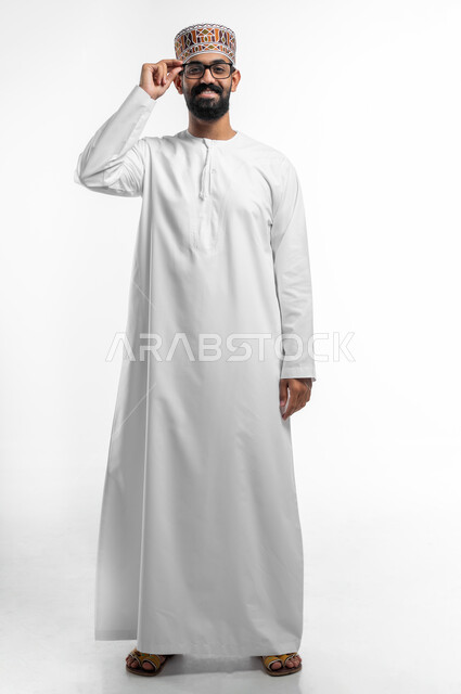 الرؤية من خلال العدسات الطبية, إيماءات السعادة و السرور بوضوح الصورة, بورتريه لشاب عربي خليجي عماني يرتدي النظارة الخاصة بضعف النظر ،مفهوم تحسين الرؤية و محاولة تعديل البصر, صورة الجسم بالطول الكامل, خلفية بيضاء