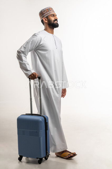 تعابير المشي و الذهاب الى المطار, بورتريه لرجل عربي خليجي عماني مبتسم يرتدي الدشداشه و الكمه يمسك حقيبة الامتعة و ينظر الى شييء ما, إيماءات التفكير والوداع, مفهوم السياحة والرحلات الترفيهية, الجسم بالطول الكامل, خلفية بيضاء