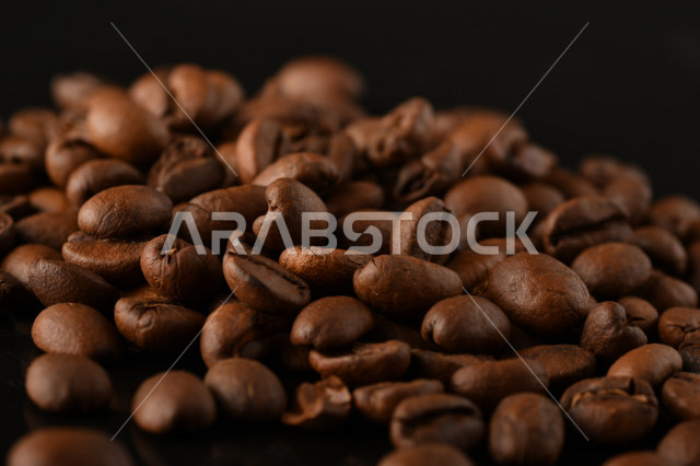 تناثر حبوب البن المحمصة على خلفية داكنة , حبوب بن القهوة البنية العضوية .