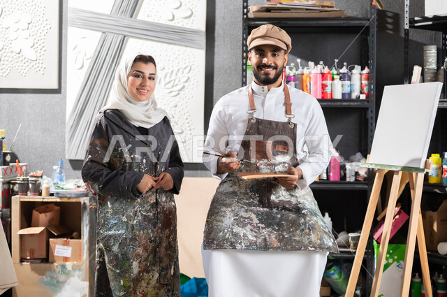 ورشة عمل فنية , استخدام أدوات و معدات الرسم و التلوين , رسام و رسامة عربيان خليجيان سعوديان يقومان بالتعاون على إنجاز مشروع فني ناجح , النظر إلى الكاميرا بإيماءات الفرح و السرور