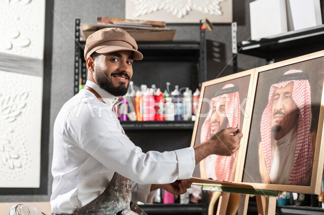 مفهوم الموهبة و الإبداع , الفخر و الاعتزاز بالانتماء للوطن العربي السعودي , لوحات فنية للعائلة السعودية المالكة , رسام عربي خليجي سعودي يرتدي الثوب التقليدي و مريلة الرسم يقدم فنون الرسم و التلوين لصور الملك سلمان و ولي العهد محمد بن سلمان , ورشة عمل فنية