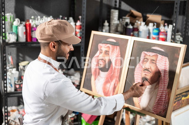 الفخر و الاعتزاز بالانتماء للوطن العربي السعودي , ورشة عمل فنية , رسام عربي خليجي سعودي يرتدي الثوب التقليدي و مريلة الرسم يقدم فنون الرسم و التلوين لصور الملك سلمان و ولي العهد محمد بن سلمان , معرض الرسومات و اللوحات التشكيلية في السعودية