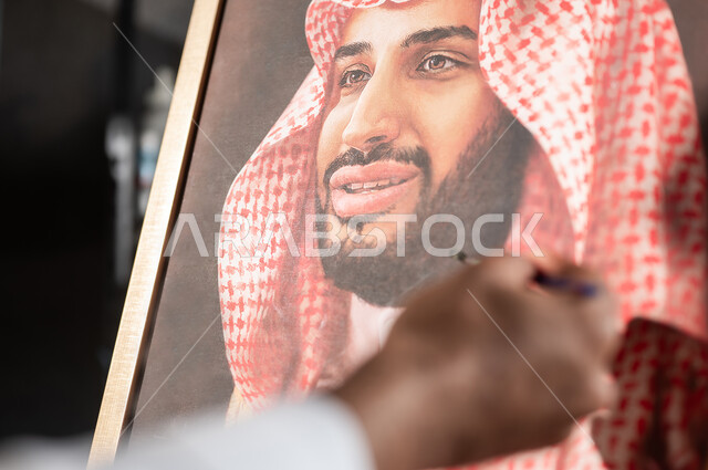 معرض الرسومات و اللوحات التشكيلية في السعودية , الفخر و الاعتزاز بالانتماء للوطن العربي السعودي , ورشة عمل فنية , صورة مقربة ليد رسام عربي خليجي سعودي يقدم فنون الرسم و التلوين لصورة ولي العهد محمد بن سلمان