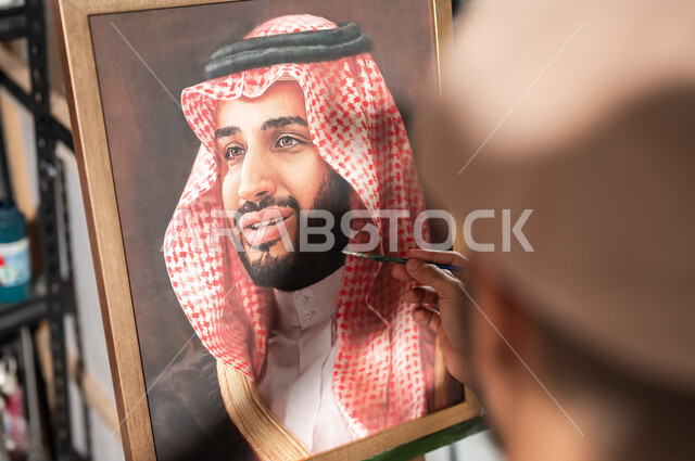 الفخر و الاعتزاز بالانتماء للوطن العربي السعودي , ورشة عمل فنية , صورة مقربة لرسام عربي خليجي سعودي يقدم فنون الرسم و التلوين لصورة ولي العهد محمد بن سلمان , معرض الرسومات و اللوحات التشكيلية في السعودية