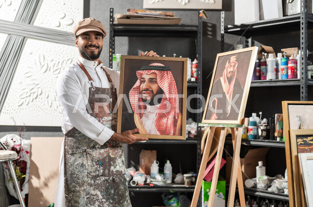 ورشة عمل فنية , الفخر و الاعتزاز بالانتماء للوطن العربي السعودي , لوحات فنية للعائلة السعودية المالكة , رسام عربي خليجي سعودي يرتدي الثوب التقليدي و مريلة الرسم يقدم فنون الرسم و التلوين لصور الملك عبد العزيز و ولي العهد محمد بن سلمان