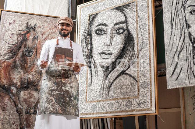 أنشطة ترفيهية فنية ممتعة , ممارسة هواية الرسم , مفهوم الموهبة و الإبداع , رسام عربي خليجي سعودي يرتدي الثوب التقليدي و مريلة الرسم يحمل أدوات و معدات التلوين بيديه , النظر إلى الكاميرا بإيماءات السعادة و السرور , معرض الرسومات و اللوحات التشكيلية في السعودية