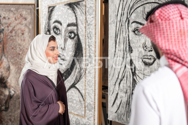الاهتمام بالفنون اليدوية , الاستمتاع بتأمل الرسوم الجدارية المعلقة , زوجان عربيان خليجيان سعوديان يقفان أمام اللوحات الفنية , الشغف بموهبة الرسم , معرض الرسومات و اللوحات التشكيلية