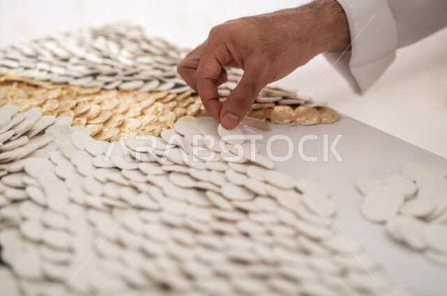 استخدام المواد المختلفة لإنشاء التصاميم المميزة , ورشة عمل فنية  , الشغف بالفنون اليدوية , صورة مقربة ليد رسام عربي خليجي سعودي يقوم بتثبيت القطع البيضاء لصغيرة على اللوحة , ممارسة هواية الرسم الجداري ثلاثي الأبعاد