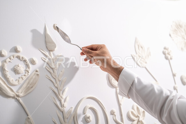 Using the appropriate tools to complete a successful art project, creating creative designs with white gypsum, a close-up of the hand of a Saudi Arabian Gulf painter practicing the art of shaping and drawing with 3D gypsum in an art workshop, fun manual recreational activities