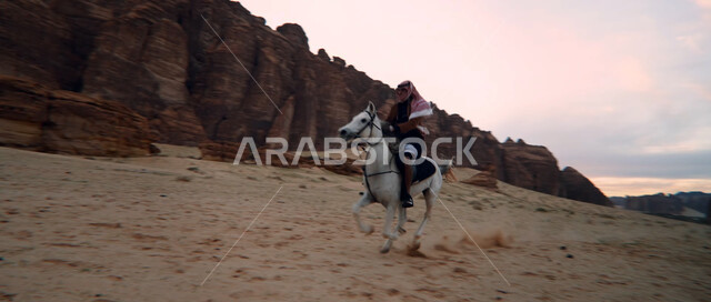 التكوينات والتشكيلات الصخرية في صحراء السعودية، إمتطاء الحصان على الرمال الناعمة في المناطق الصحراوية، توارث حب الخيول من الأجداد ونشره بين أبناء الوطن، ممارسة هواية ركوب الخيل وشغف الفروسية، رجل عربي خليجي سعودي يركب على ظهر جواد عربي أصيل