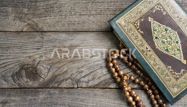 مكان مخصص للعبادة والطاعة والتقرب الى الله، المصحف الشريف وسبحة التهليل، الهداية بنور القرآن الكريم، مفهوم التمعن بآيات وسور القرآن، مسبحة يد من حبات الخرز على طاولة خشبية
