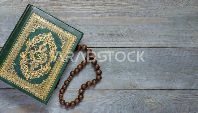 مسبحة يد من حبات الخرز على طاولة خشبية، مكان مخصص للعبادة والطاعة والتقرب الى الله، المصحف الشريف وسبحة التهليل، الهداية بنور القرآن الكريم، مفهوم التمعن بآيات وسور القرآن