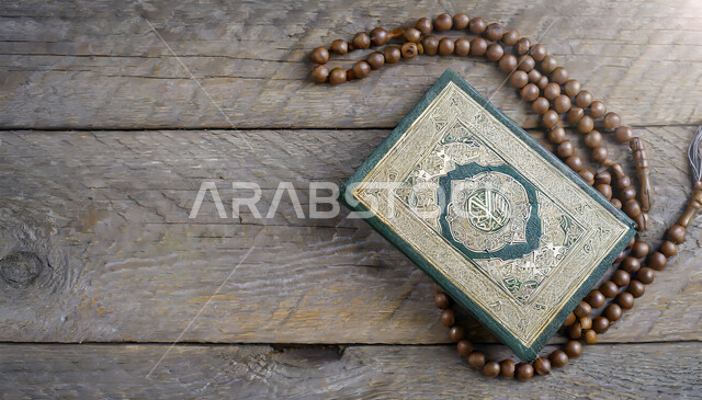 مفهوم التمعن بآيات وسور القرآن، مسبحة يد من حبات الخرز على طاولة خشبية، مكان مخصص للعبادة والطاعة والتقرب الى الله، المصحف الشريف وسبحة التهليل، الهداية بنور القرآن الكريم