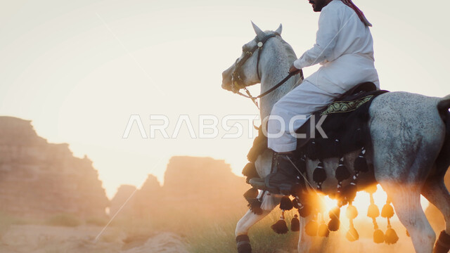 Natural rock formations and formations in the Saudi desert, following the traditions of our ancestors in caring for and raising horses, wandering through the desert nature on the back of a horse, the relationship of the people of the country with purebred horses, a Saudi Gulf Arab man riding a horse.